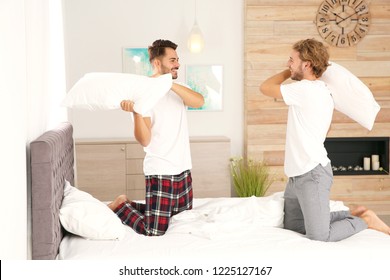 Happy Gay Couple Having Pillow Fight On Bed At Home