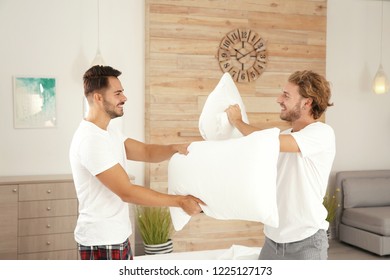 Happy Gay Couple Having Pillow Fight On Bed At Home