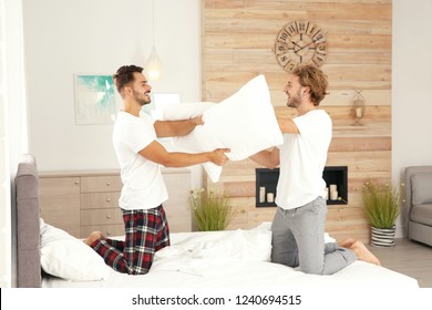 Happy Gay Couple Having Pillow Fight On Bed At Home