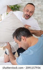 Happy Gay Couple Having Pillow Fight On Bed At Home