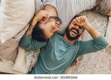 Happy Gay Couple Lying Down On The Bed At Home, Hugging And Flirting.