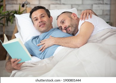 Happy Gay Couple Reading Book On Bed