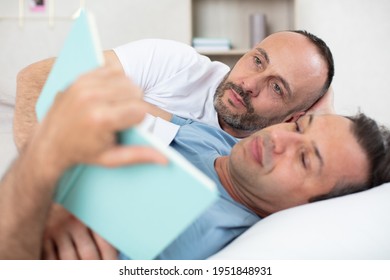 Happy Gay Couple Reading Book On Bed