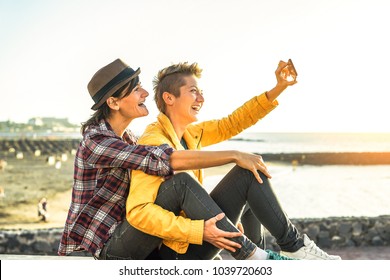 Happy Gay Couple Taking A Selfie With Mobile Smart Phone Camera On The Beach At Sunset - Lesbians Having Fun In Holiday - Homosexuality, Diversity, Vacation, Travel, Lgbt, Technology Concept