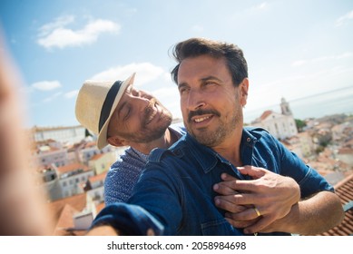 Happy gay couple taking selfie on balcony. Two men in casual clothes looking at each other, city in background. Love, affection, relationship, travelling concept - Powered by Shutterstock