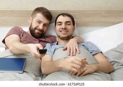 Happy Gay Couple Watching TV In Bed At Home