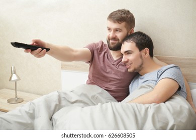 Happy Gay Couple Watching TV In Bed At Home