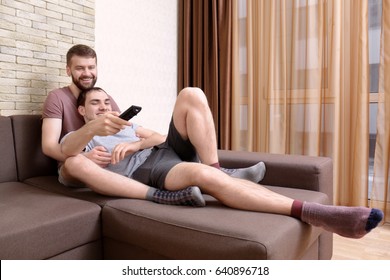 Happy Gay Couple Watching TV On Sofa At Home