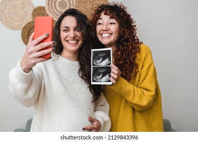 Happy gay couple of women holding ultrasound photo scan on video call - Growing baby in pregnancy time concept