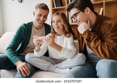 Happy Gay Family Smiling And Using Mobile Phone While Sitting On Couch At Home