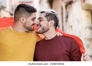 Happy Gay Male Couple Kissing Wearing Rainbow LGBT Flag At Pride Event - LGBTQ Love Concept