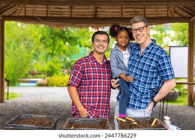 Happy gay man couple and little daughter learning to farm earthworms to using their castings as a nutrient-rich fertilizer for crops. Diversity LGBTQ family spending time together to gardening at home - Powered by Shutterstock