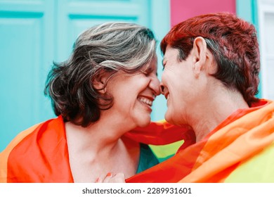 Happy gay senior lesbian couple wearing lgbt rainbow flag outdoors - Diversity family love - Main focus on right woman head