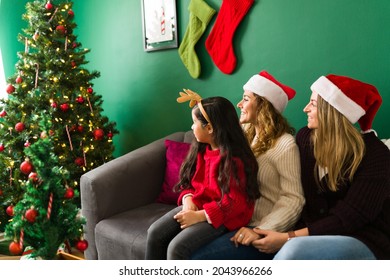 Happy Gay Women Looking Proud At The Family Christmas Tree. Cute Girl Finishing Putting Up A Decorated Tree With Her Two Moms