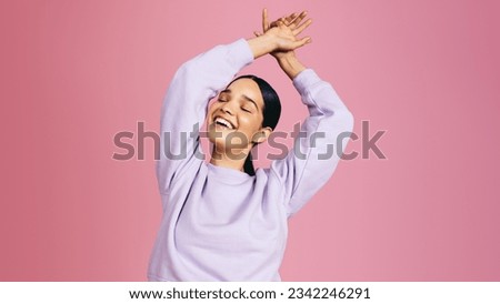 Happy gen z female radiating positivity as she dances and celebrates in the studio. She is wearing casual clothing and minimal makeup, feeling vibrant and confident in herself.