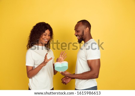 Happy to get gift. Valentine's day celebration, happy african-american couple isolated on yellow studio background. Concept of human emotions, facial expression, love, relations, romantic holidays.