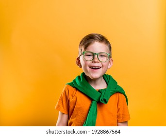 Happy Ginger Boy With Freckles On Saint Patrick Day. Kid In Green Glasses And Orange T-shirt. Patrick Party With Irish Culture And Traditions. Bright Child Boy With Leprechaun For A St. Patrick's Day