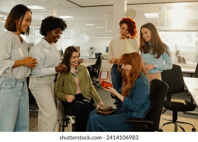 Happy ginger business woman opening a gift while celebrating birthday with multiracial coworkers in the office. Diverse business people making a surprise party for their coworker. Copy space. - Powered by Shutterstock