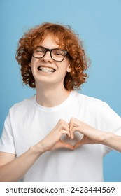 Happy ginger curly boy showing heart shape for subscribers isolated on blue background. Positive lifestyle, social media concept 