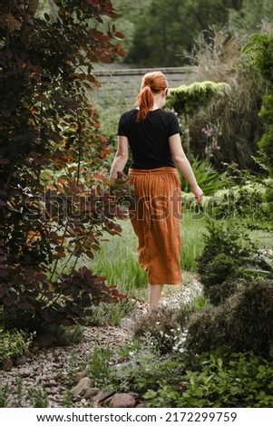 Happy ginger hair woman walking barefoot in the park or garden. Freedom and healthy way of life. Female in her 40s having rest outdoors. People in motion, move Cheerfully person in well-groomed garden