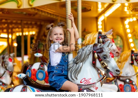 happy girl in an amusement park rides a horse on a carousel in the summer