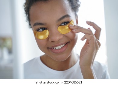 Happy Girl Is Applying Eye Patches. Skin Moisturizer With Collagen Serum. Beauty Routine Of Lovely Teenage African American Girl. Mirror Reflection Of Young Spanish Woman Face. Morning Skincare.