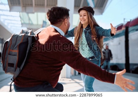 Happy girl with arms outstretched running into father's embrace at the station.