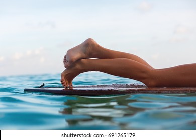 Happy girl in bikini have fun before surfing Surfer lie on surf board. Close up bare legs. People in water sport adventure camp, extreme activity on family summer beach vacation. Watersport background