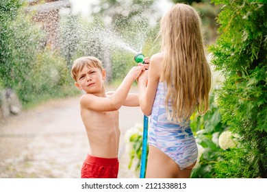 Happy Girl And Boy Playing With Water In Summer. Children Having Garden Hose Fun In Back Yard