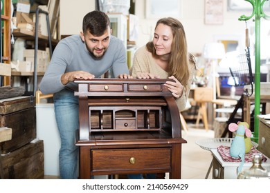 Happy girl with boyfriend choosing vintage cabinet in furnishings store - Shutterstock ID 2140569429