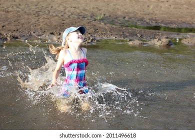 happy girl in a bright swimsuit runs into the river, splashes and splashes around, active holidays with children on the beach in summer