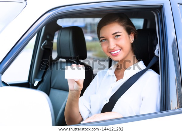 Happy girl in a car showing an empty white card\
for your message
