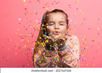 Happy girl celebrating on a pink background. Blows up multicolored confetti - Powered by Shutterstock