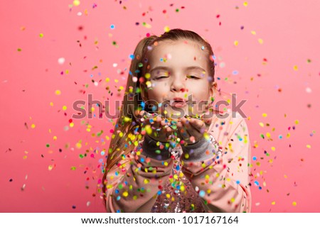 Happy girl celebrating on a pink background. Blows up multicolored confetti