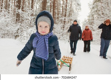 Happy girl child with family walk in winter snowy forest. Grandparents and parents have fun with wooden sled in winter.