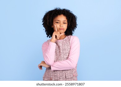 A happy girl with curly hair poses thoughtfully against a soft blue backdrop. Her playful yet serious expression reflects youthful curiosity and imagination, capturing a moment of childhood fun. - Powered by Shutterstock