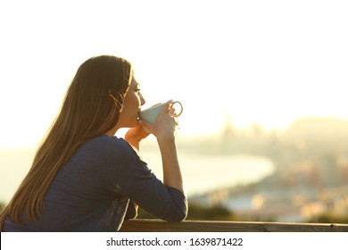 Happy girl drinking coffee contemplating views from a balcony at sunset - Powered by Shutterstock