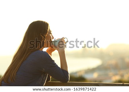 Happy girl drinking coffee contemplating views from a balcony at sunset