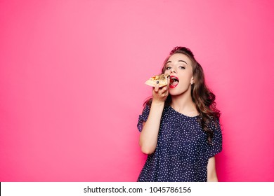 Happy girl eating a pizza. She opened her mouth, holding a pizza in her right hand and staring at you with satisfaction. Isolated on pink background - Powered by Shutterstock