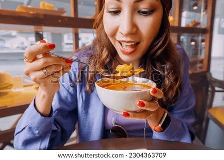 Happy girl eating spicy thai soup Tom Yam in authentic restaurant