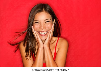 Happy girl excited. Young woman smiling very happy surprised holding head being amazed on red background. Funky young multicultural Caucasian / Chinese Asian female model joyful on red background. - Powered by Shutterstock