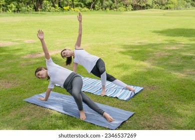 A happy girl exercising training in yoga and looking at the female instructor next to her in the park - Powered by Shutterstock