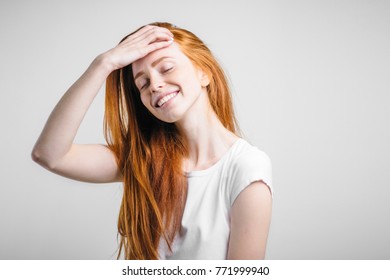 Happy girl with freckles smiling with closed eyes touching her red hair over white background.