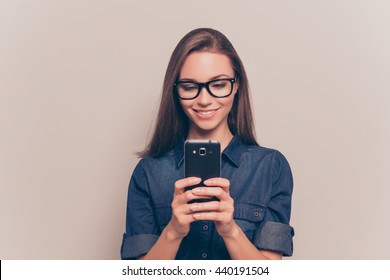 Happy girl in glasses typing sms on gray background
