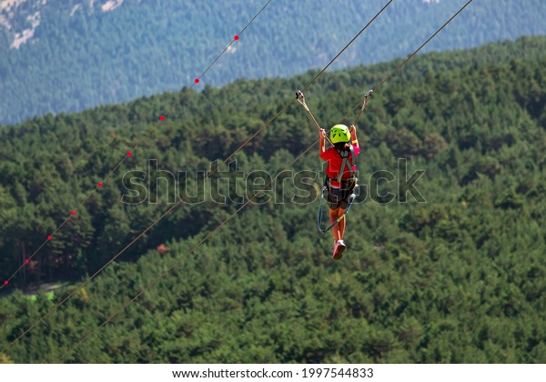 Happy girl gliding climbing in\
extreme road trolley zipline in forest on carabiner safety link on\
tree to tree top rope adventure park in Pyrenees of\
Andorra