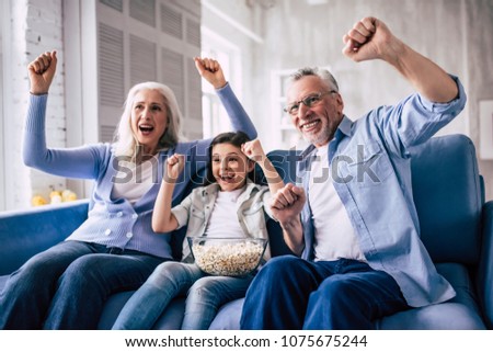The happy girl and grandparents wathing television and gesturing