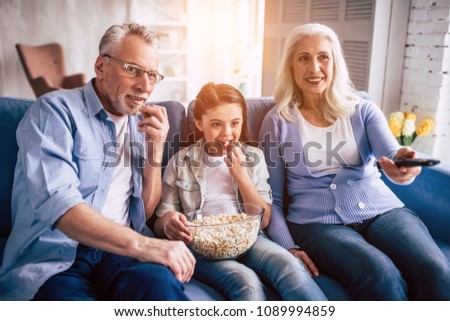 The happy girl and grandparents wathing television with a popñorn