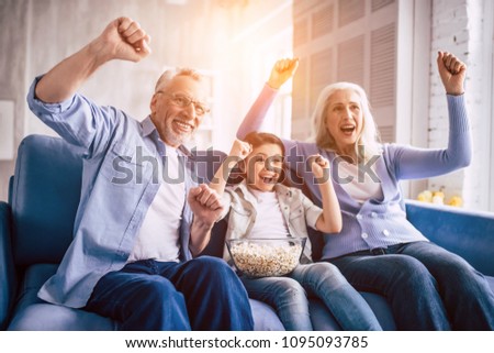 The happy girl and grandparents wathing television and gesturing