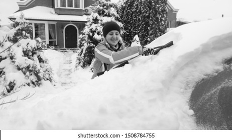 Happy Girl In Green Sport Coat Cleaning A Snow Covered White Car After Blizzard With Brush