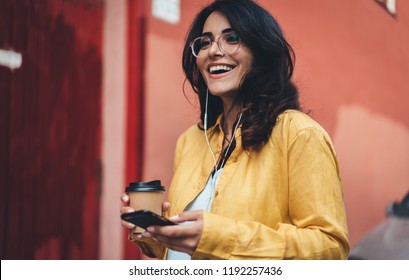 Happy girl in hipster eyeglasses listening to music while going to work, cheerful hispanic woman drinking coffee outdoors using modern smartphone device, happy smiling european businesswoman walking - Shutterstock ID 1192257436
